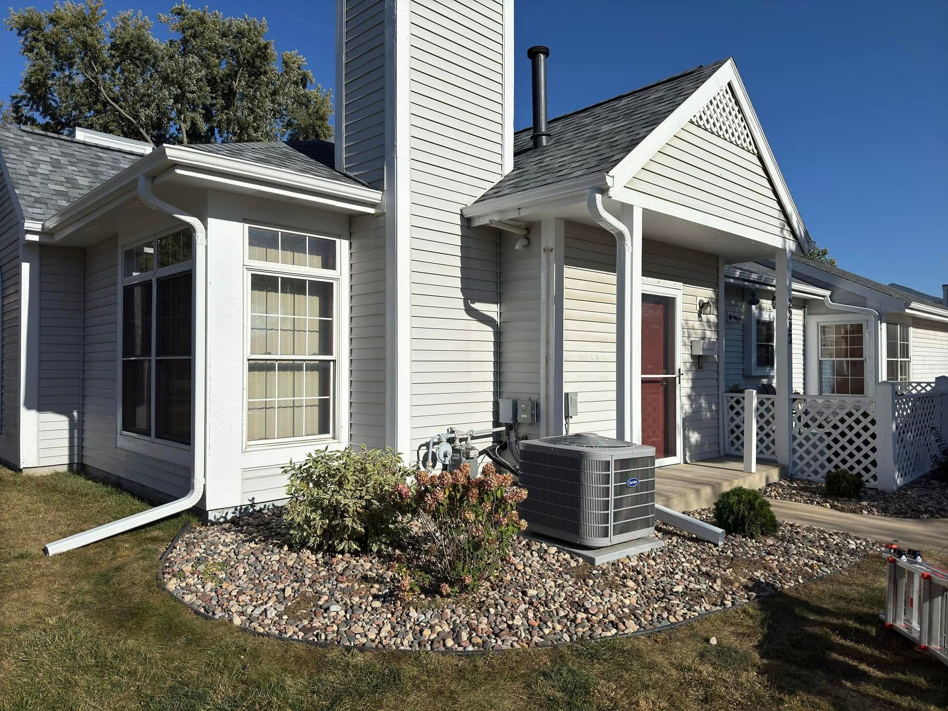 Light gray residential building with white trim, a small garden, and air conditioning unit.