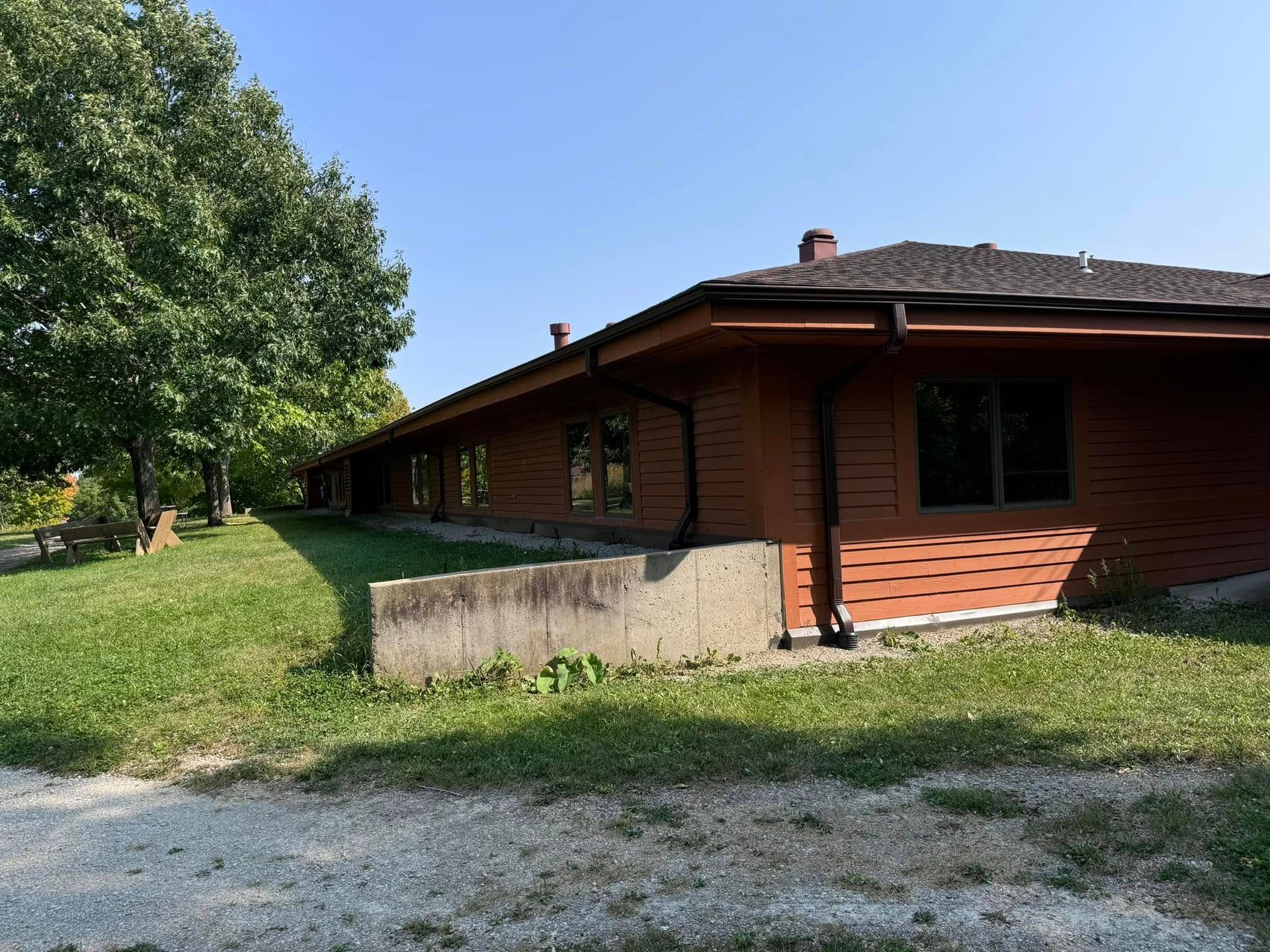 Brown building with multiple windows and a concrete wall next to a grassy lawn on a sunny day.