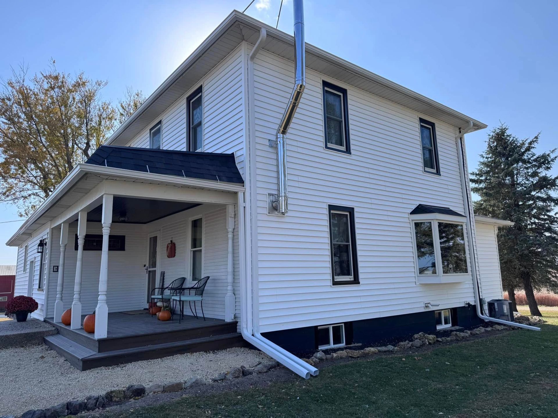 White two-story house with black trim, porch, and chimney. Sunny outdoor setting.