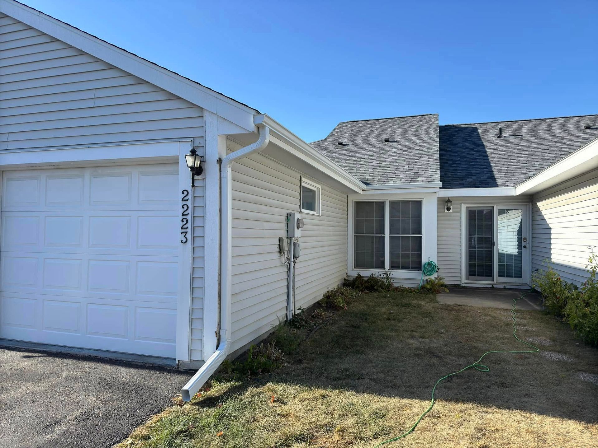A beige house with a white garage door, front door, and a brown lawn under a clear, blue sky.