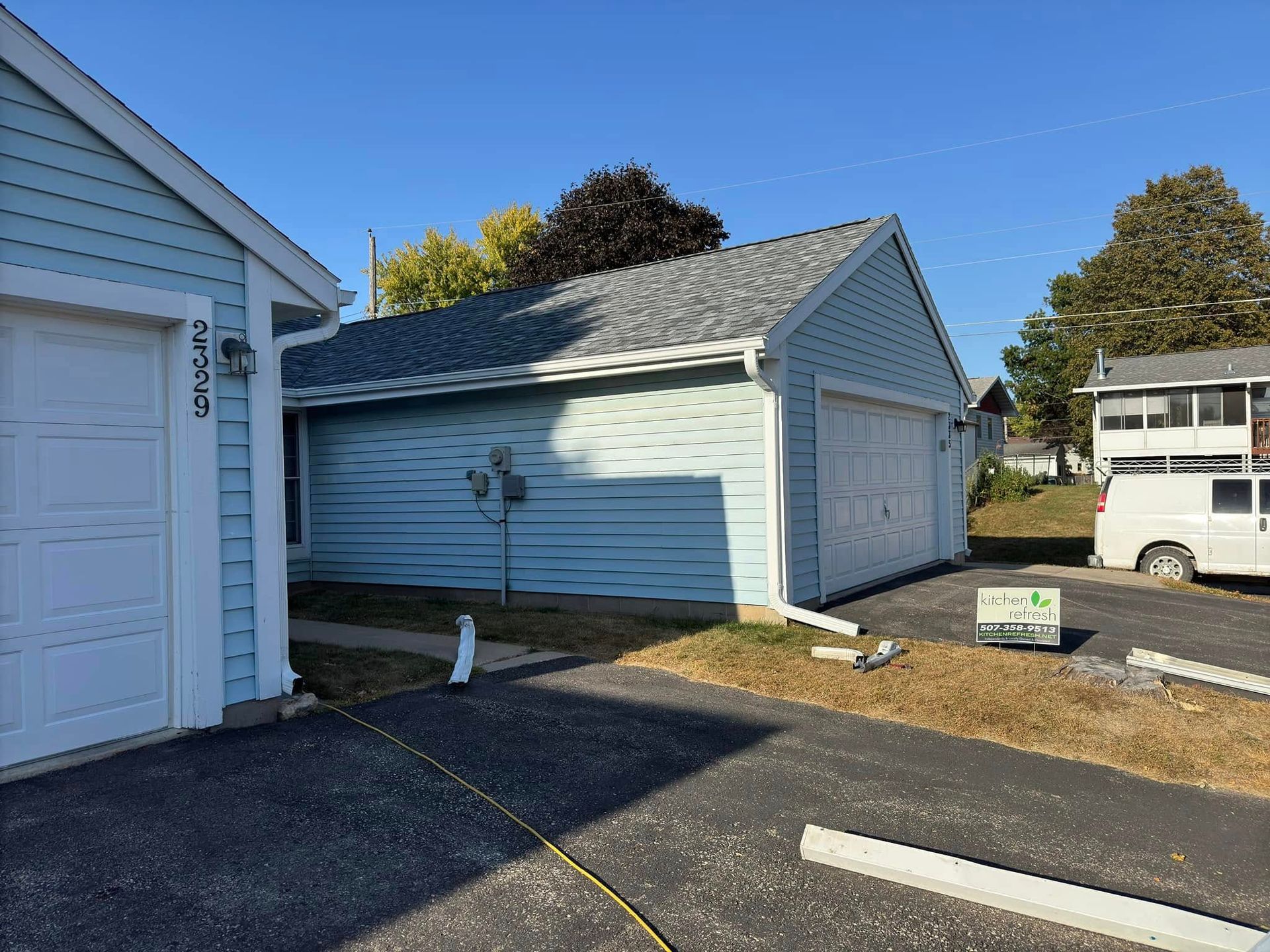 Light blue garage with white doors, gray roof, on a sunny day.