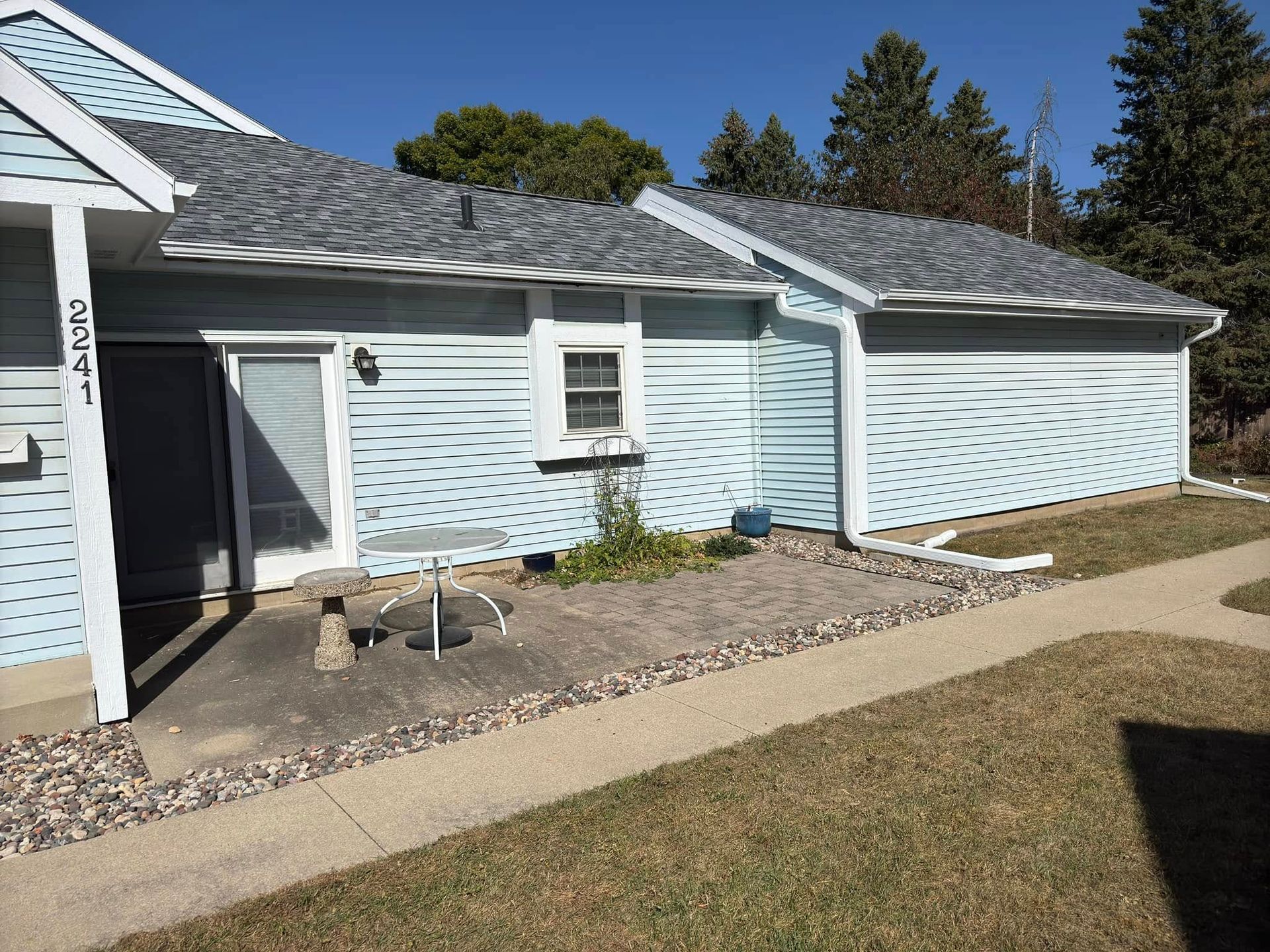 Light blue townhome with gray roof, small patio, and path in front.