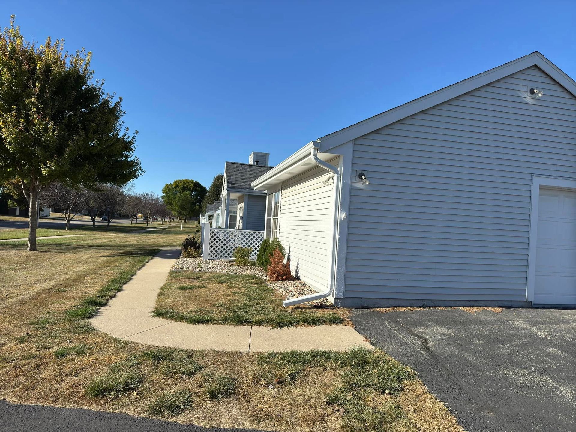 Side view of a light gray house with a pathway and grassy yard on a sunny day.