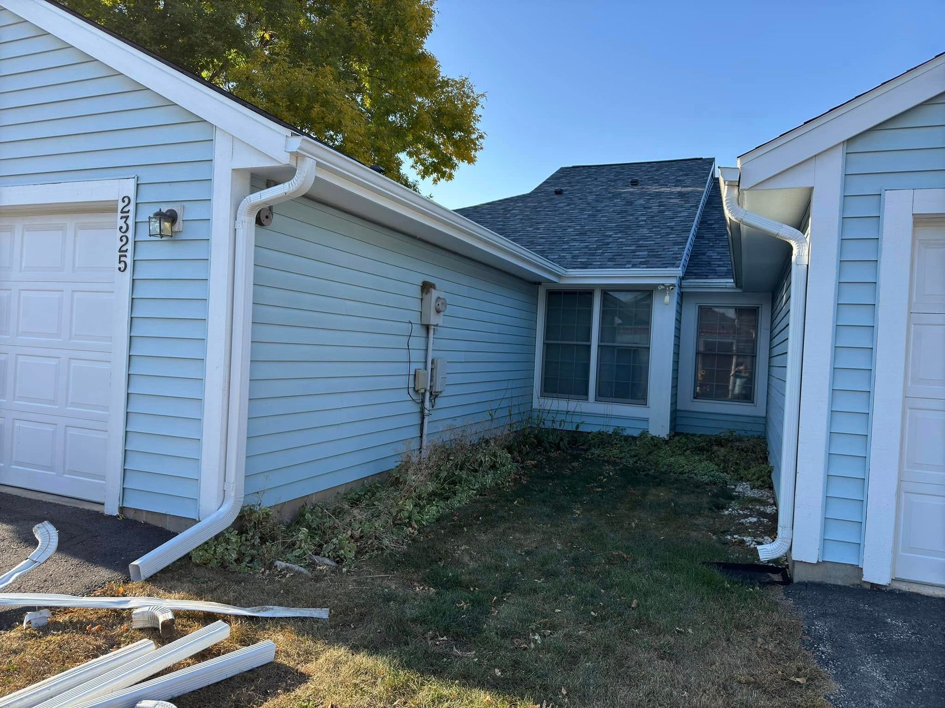 Blue siding on a house with white gutters, a garage, and overgrown grass in front.