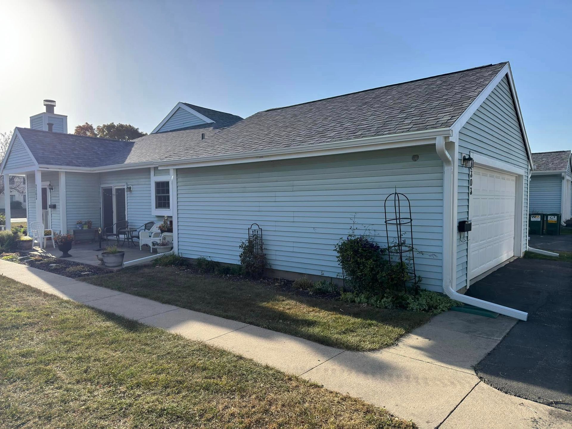 Light blue house with attached garage, sidewalk, and green lawn under a blue sky.