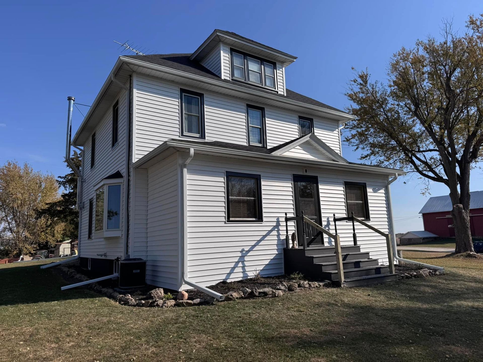 White two-story house with dark trim and a black roof on a sunny day.