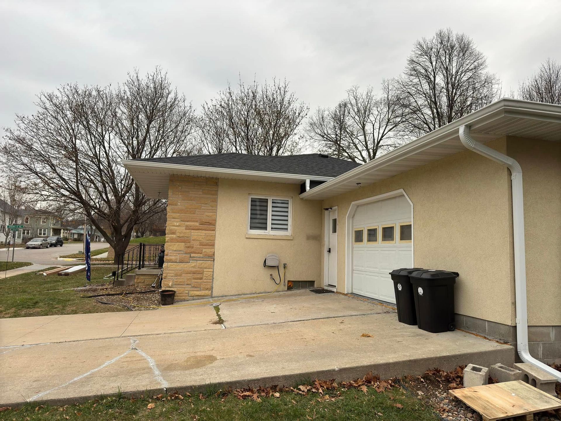 Tan stucco house with attached garage, concrete driveway, and overcast sky.