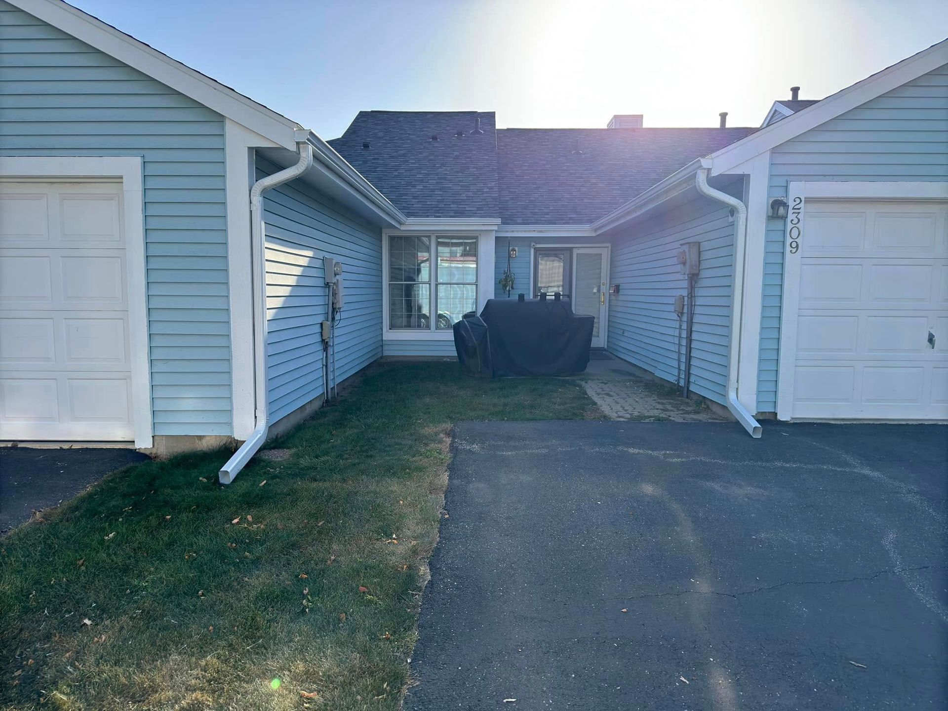 Light blue townhouses with garages, a walkway, and a small yard on a sunny day.