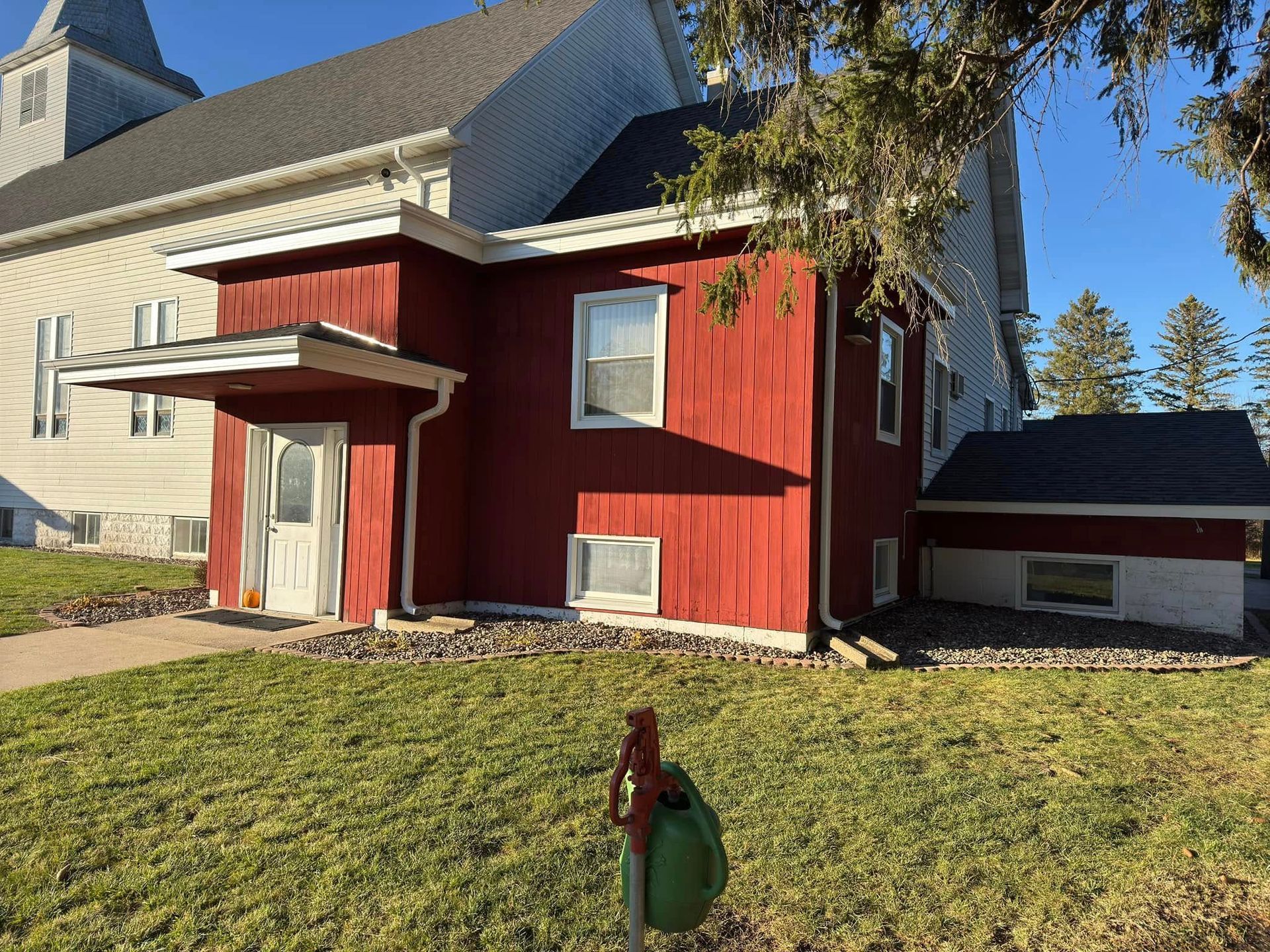 Red building attached to a white church with green grass in front.