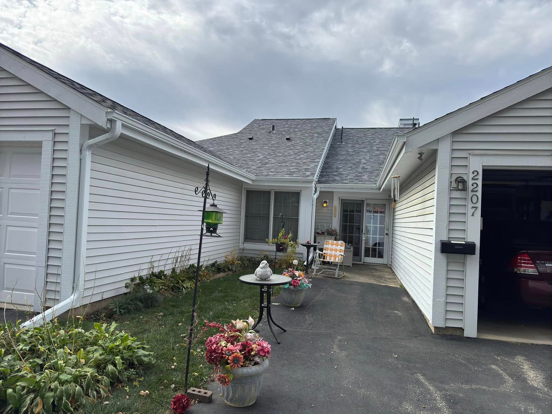 Exterior view of a white house with a driveway. Flowers and a table decorate the front entrance, overcast sky.