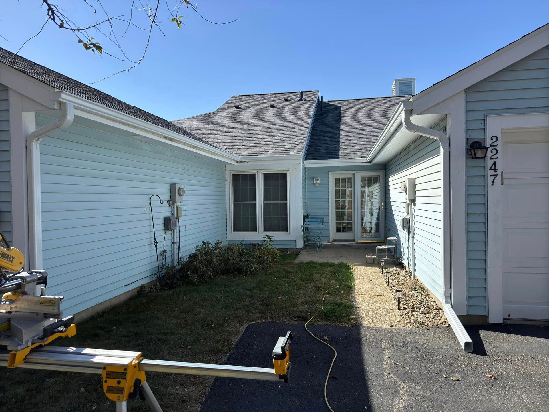 Blue house with white trim, driveway, and front door. A saw is in the foreground.