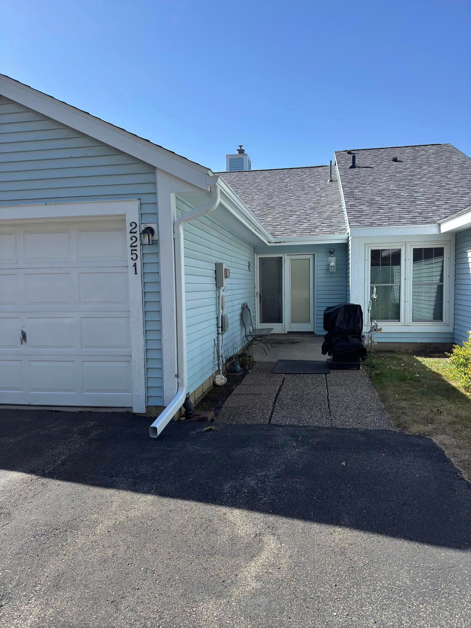 Light blue house with white garage door and dark asphalt driveway.