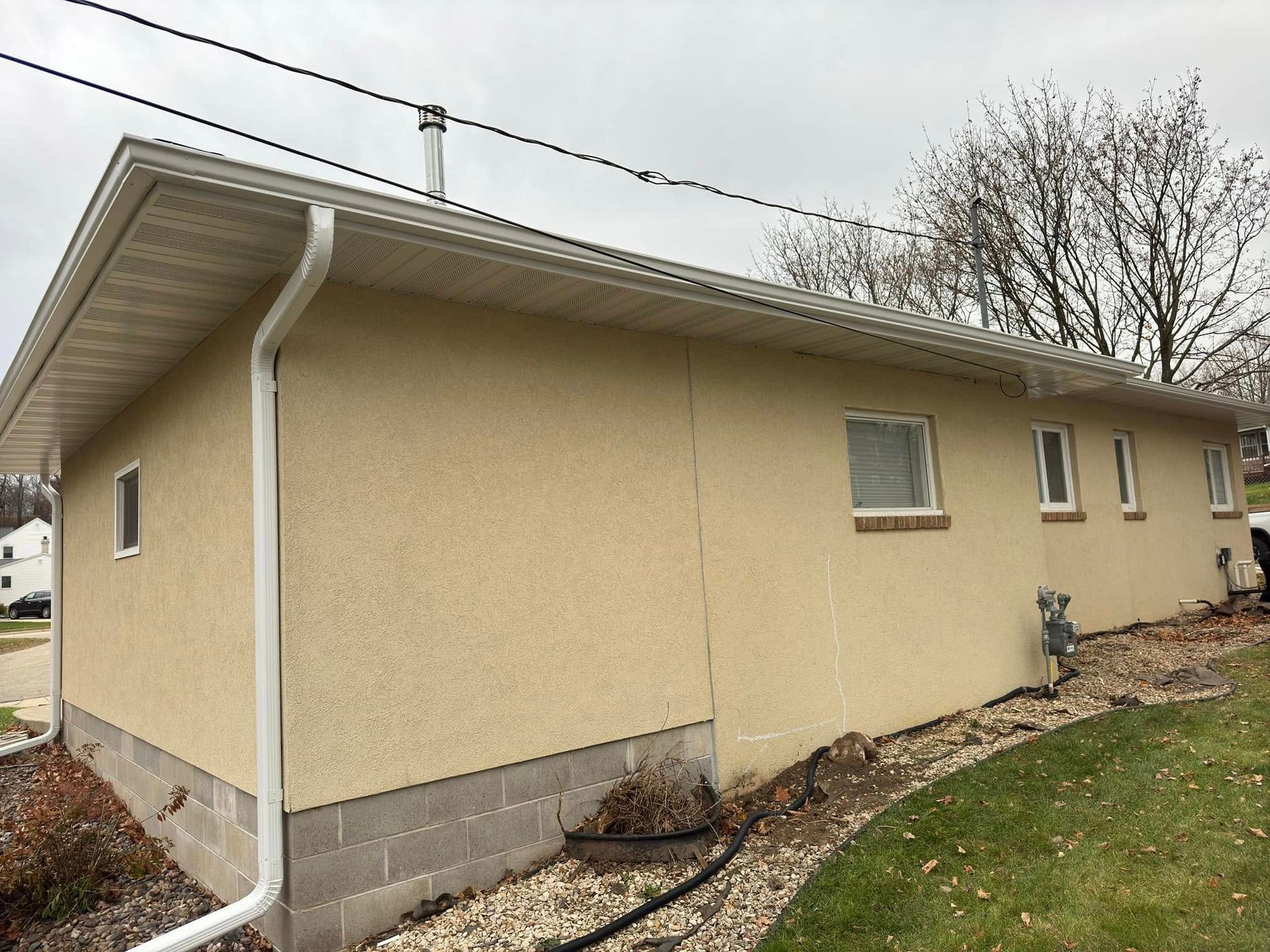 Tan stucco house with white trim, gutters, and windows. Overcast day.