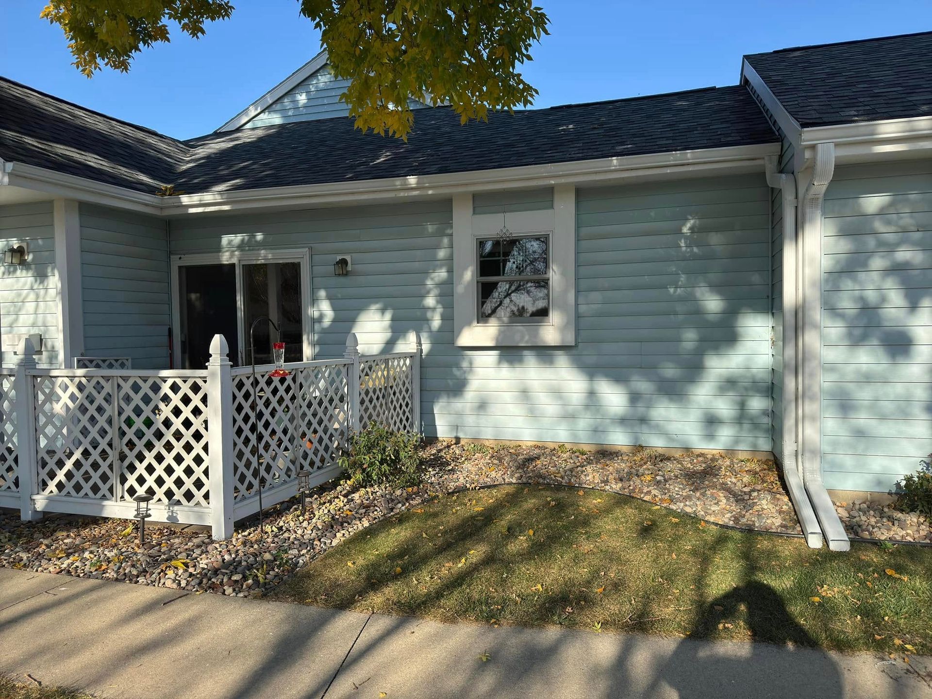 Light blue building with a white lattice fence, small window, and green lawn.