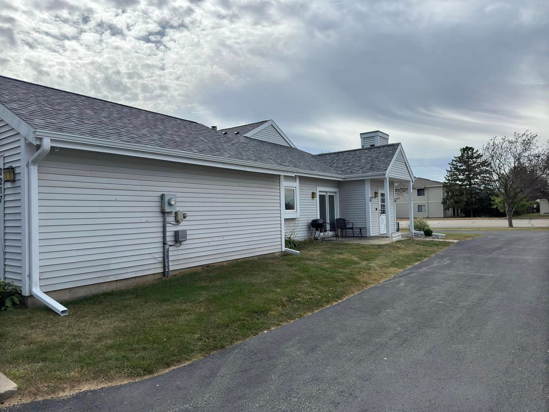 Gray building with white trim, gray roof, and a paved walkway, under a cloudy sky.