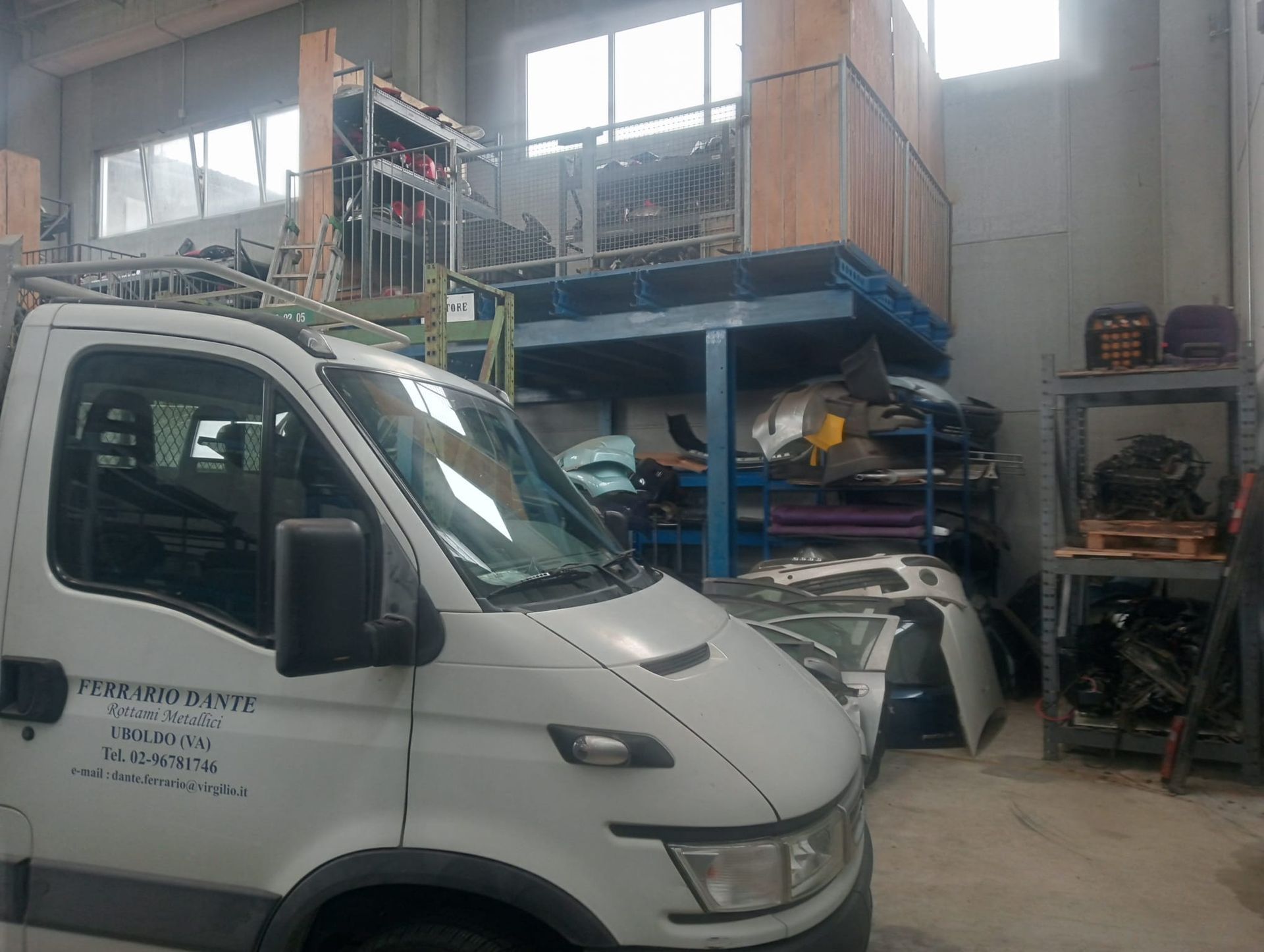 Un furgone bianco è parcheggiato in un magazzino pieno di pezzi di ricambio.