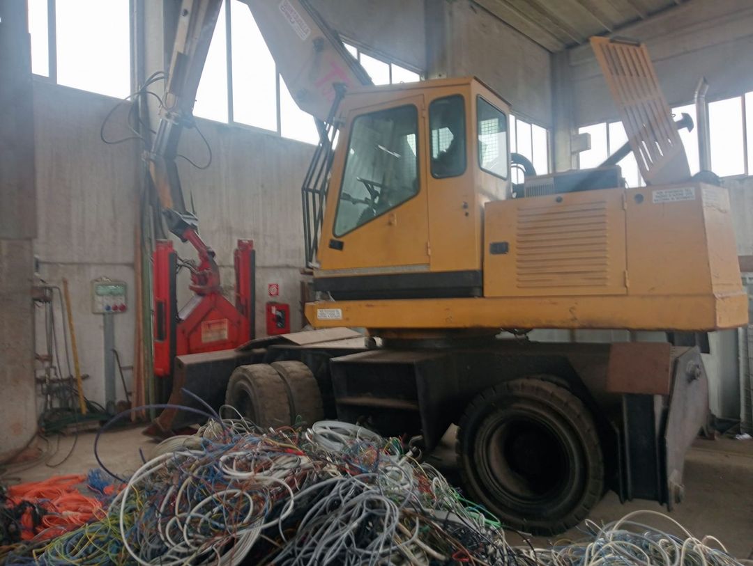 Un escavatore giallo è parcheggiato in un magazzino accanto a una pila di cavi.