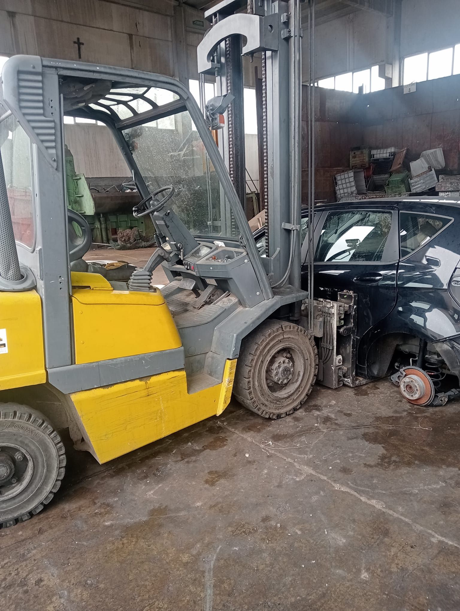 Un carrello elevatore giallo è parcheggiato accanto a un'auto nera in un garage.
