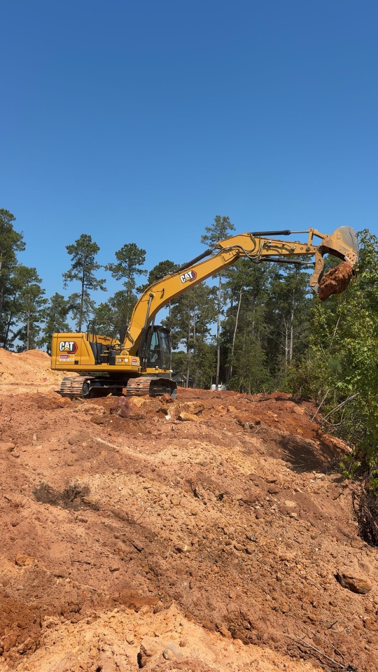 Dirt-filled stream bed with a culvert, surrounded by rocks, bare trees, and a sunny sky.