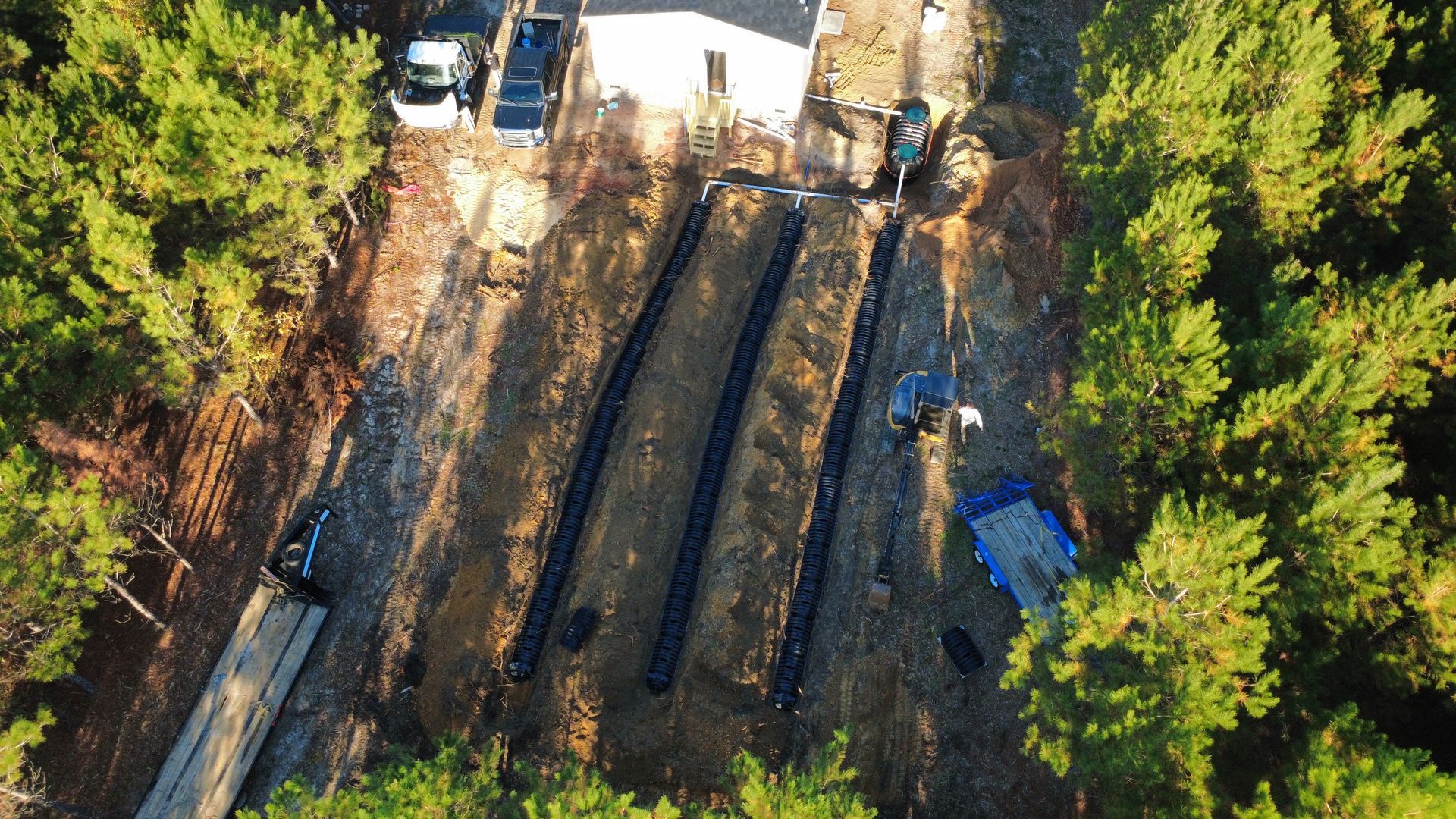 Black septic tank in dirt, with blue pipe and access lid, near a concrete structure.