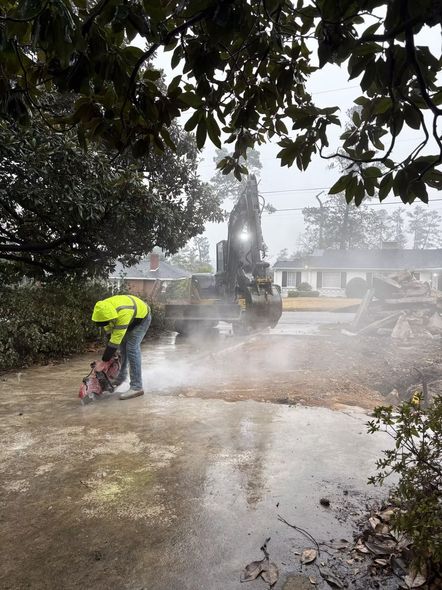 Man in yellow safety vest using saw to cut pavement; construction site.