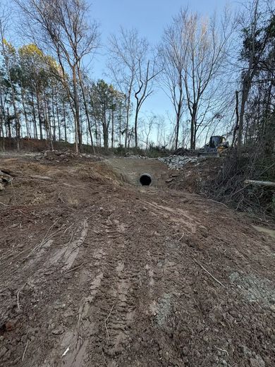 Dirt hillside leading to a black culvert, trees in the background.