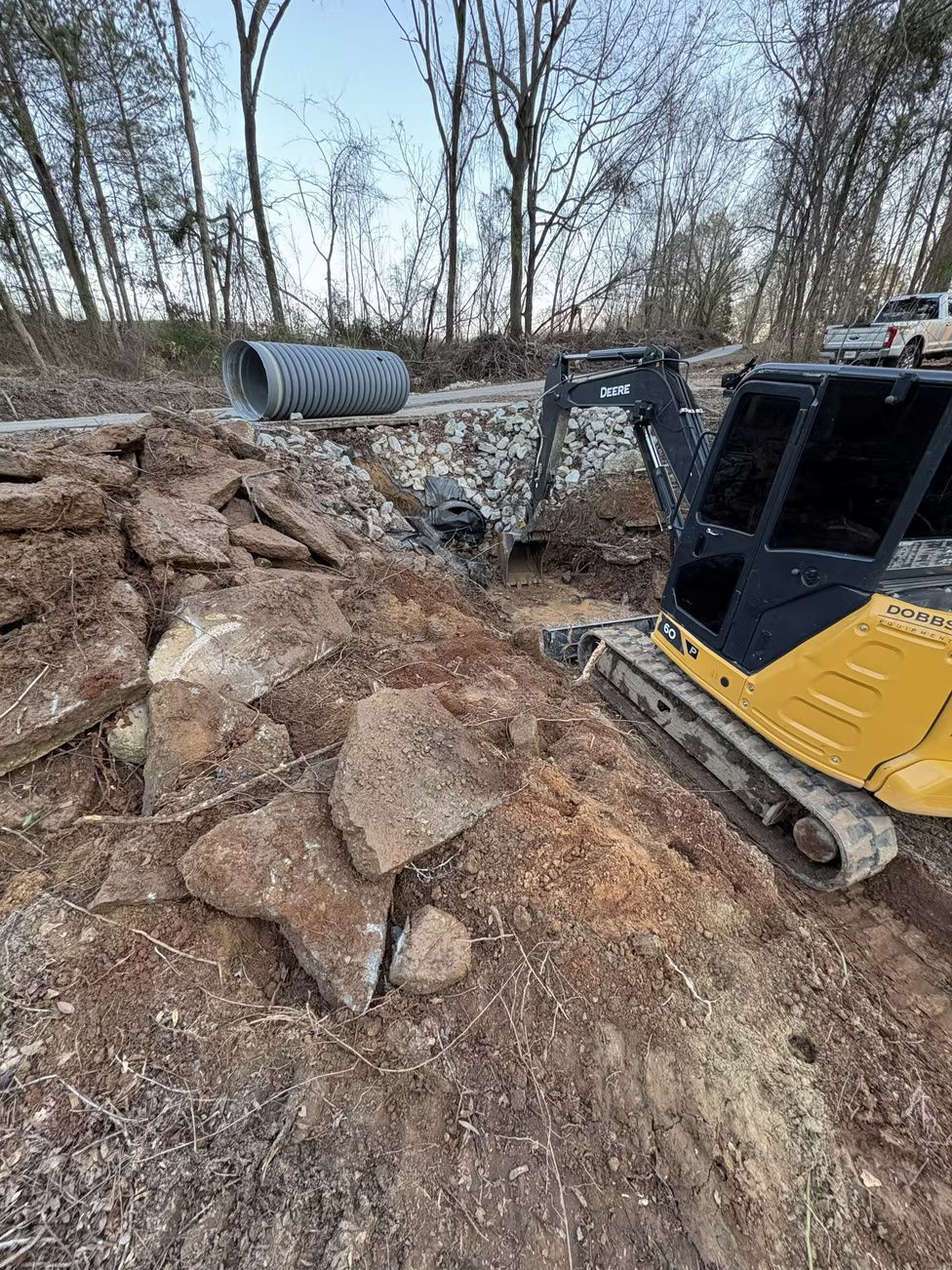 Yellow excavator working on a construction site with large stones, dirt, and a culvert pipe.