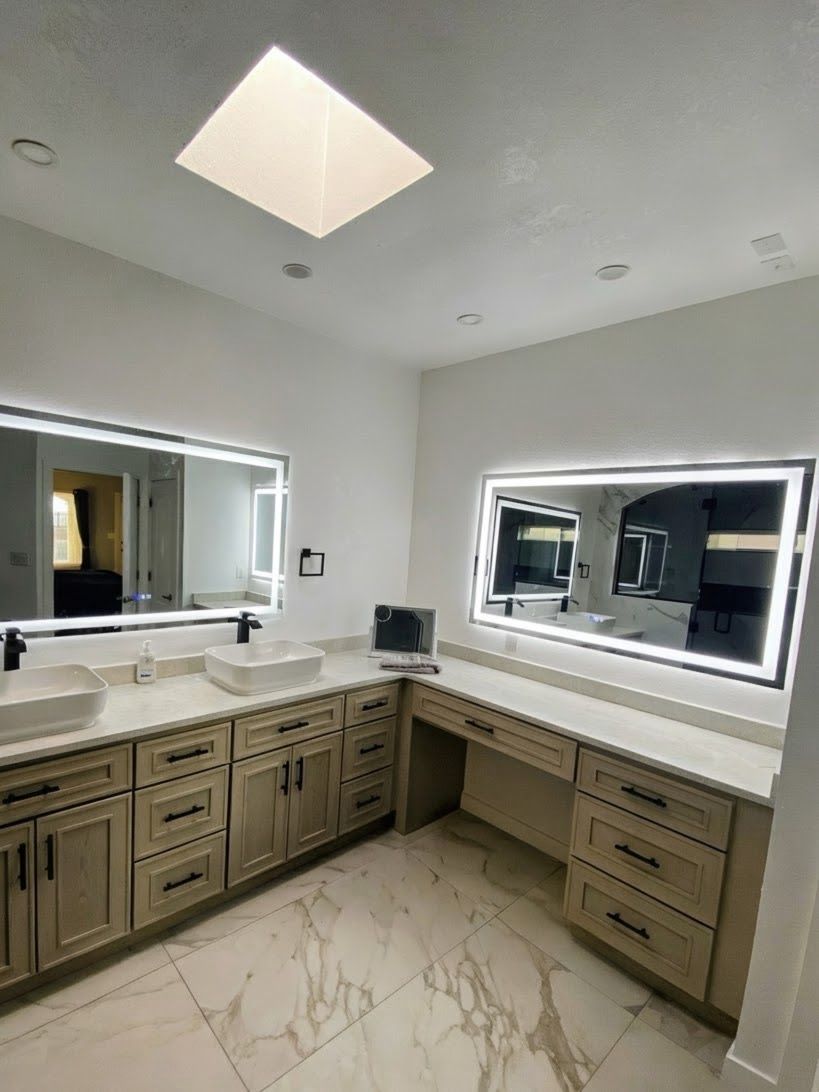 Spacious bathroom with two vanity areas, mirrors with LED lights, neutral tones, and a skylight.