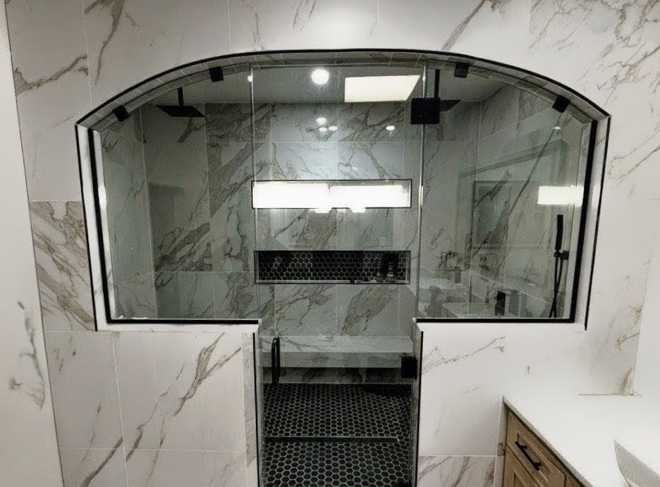 A luxurious bathroom with arched glass shower enclosure. White marble tile, black fixtures, and a modern design.
