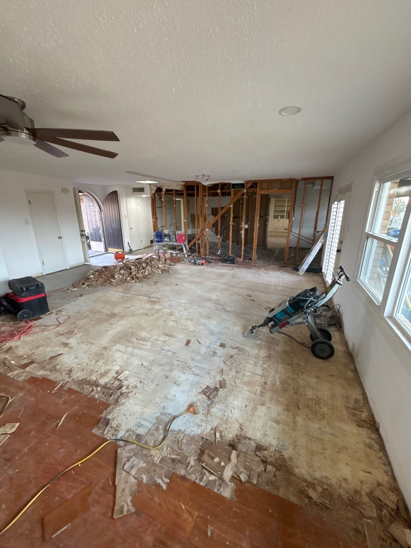 Interior room undergoing renovation; exposed studs, flooring removed, power tools, doorway, and windows.