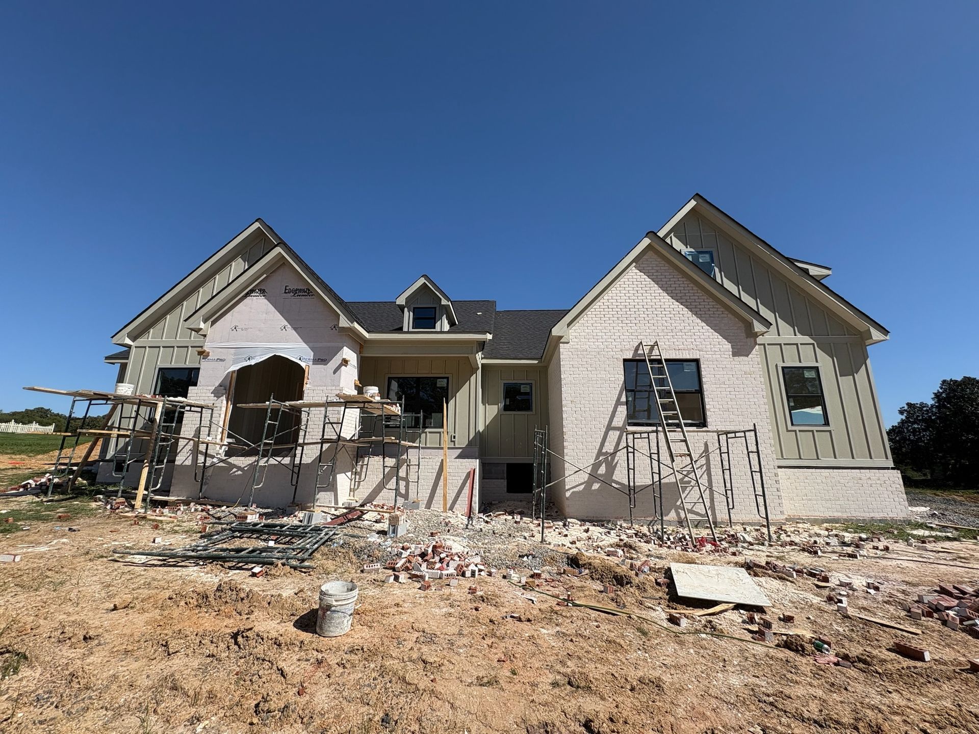 A large white house is being built in a dirt field.