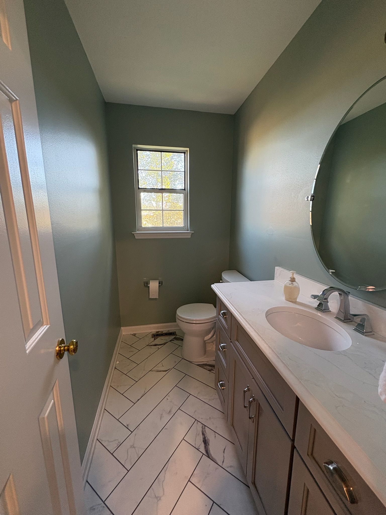 A bathroom with a toilet , sink , mirror and window.