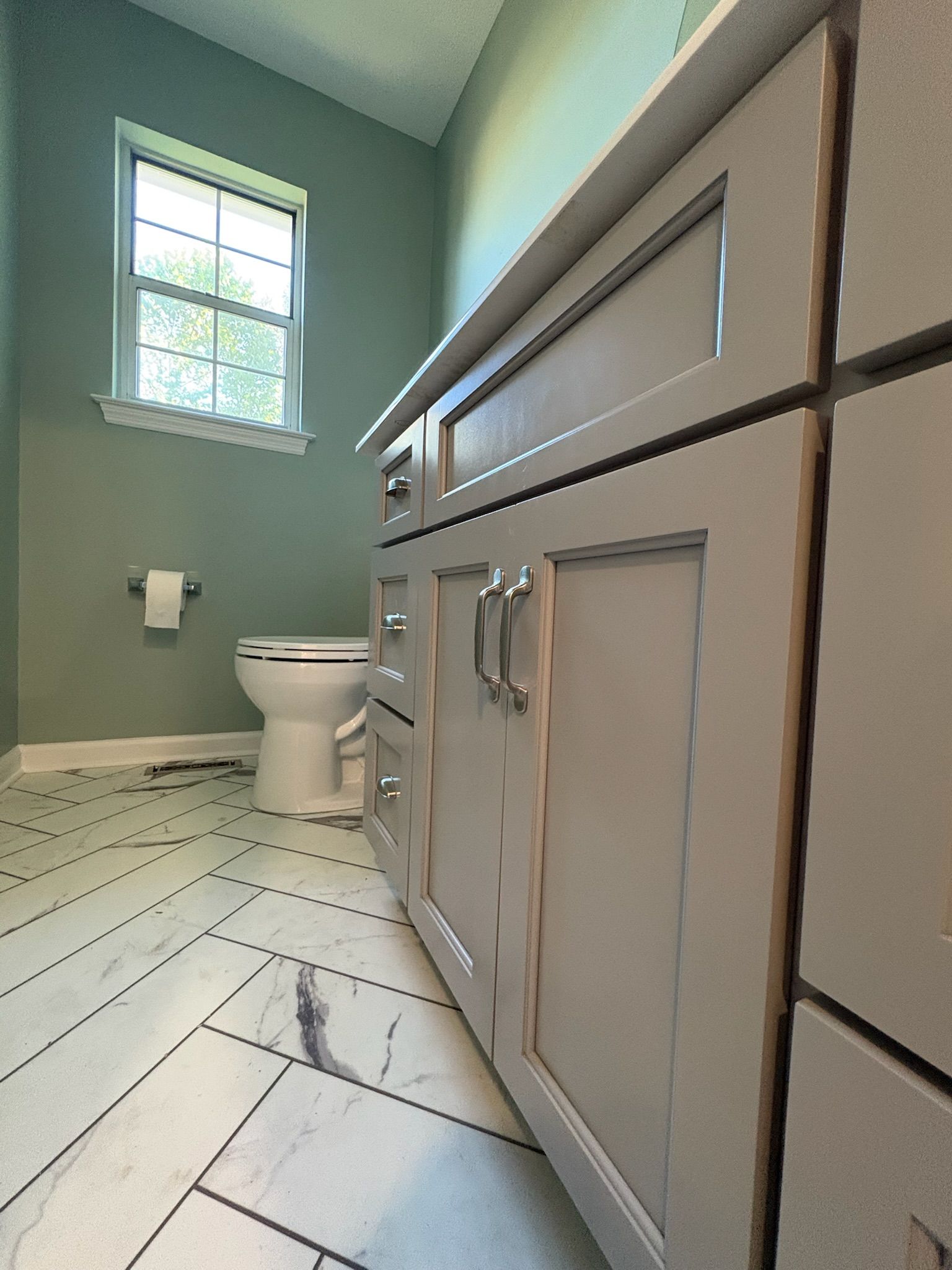 A bathroom with a toilet , sink , cabinets and a window.