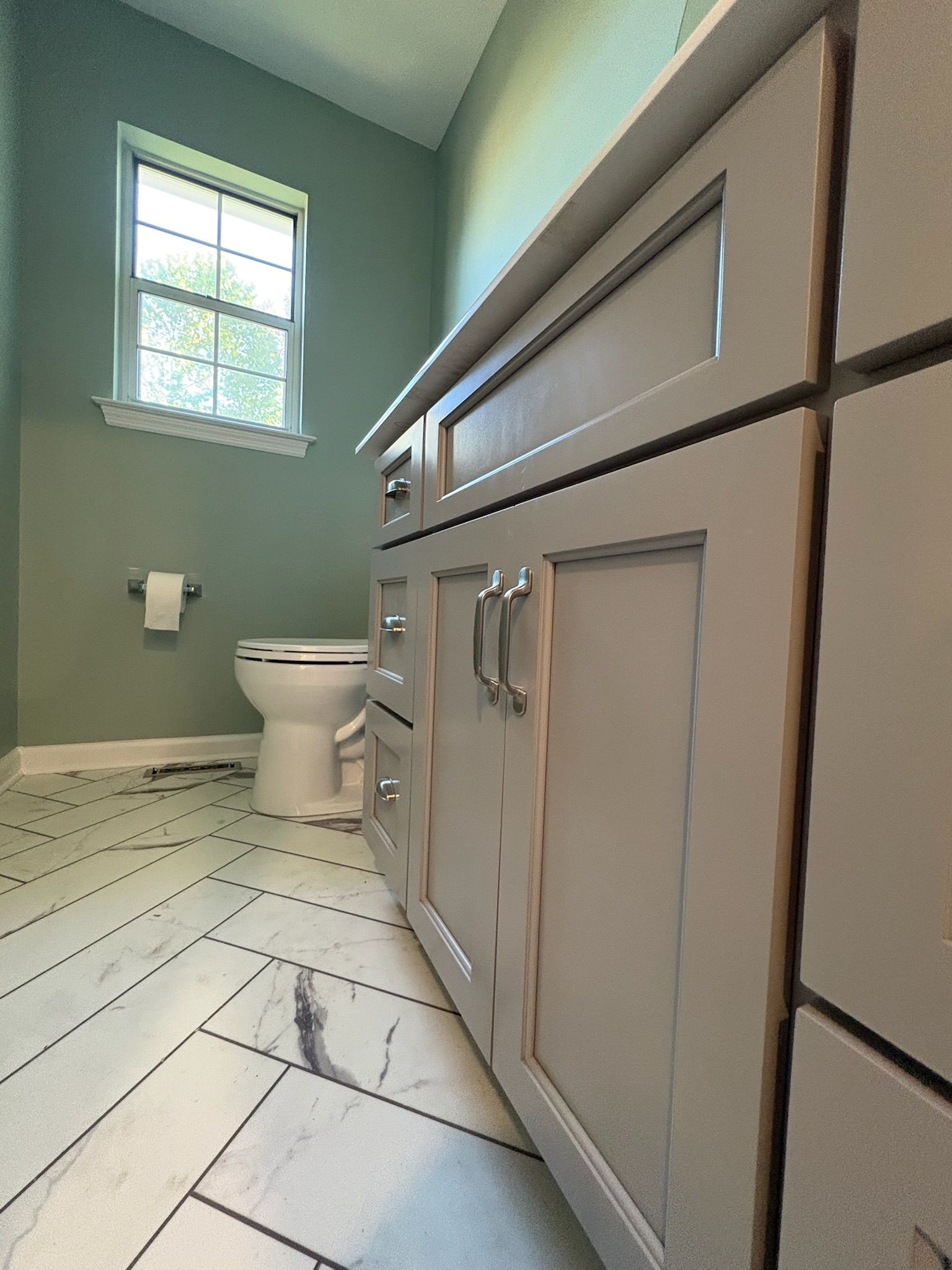 A bathroom with a toilet , sink , cabinets and a window.