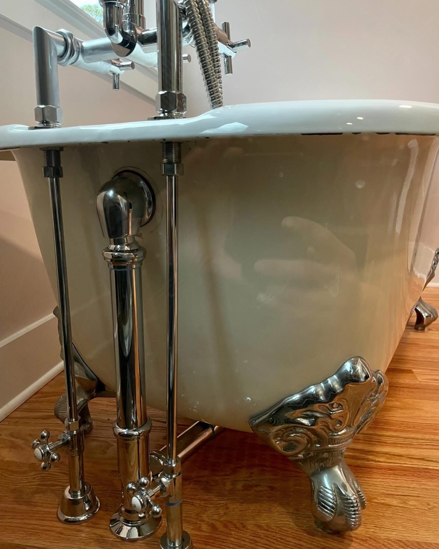 A white bathtub with chrome legs is sitting on a wooden floor.