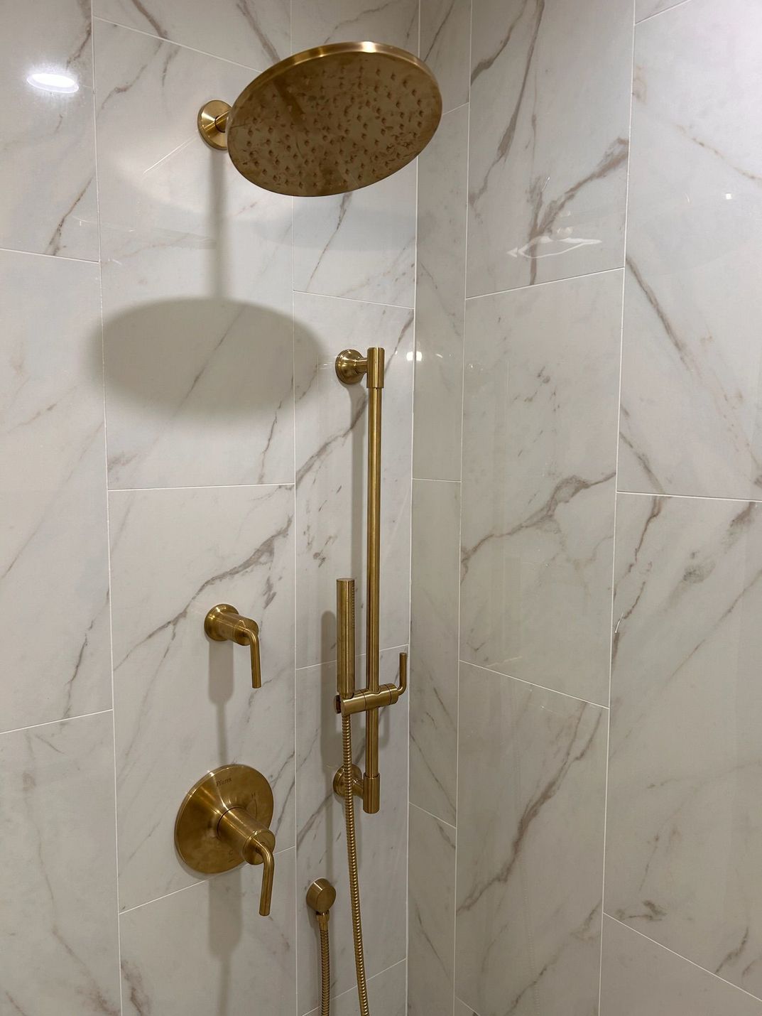 A shower with a gold shower head and a marble wall.