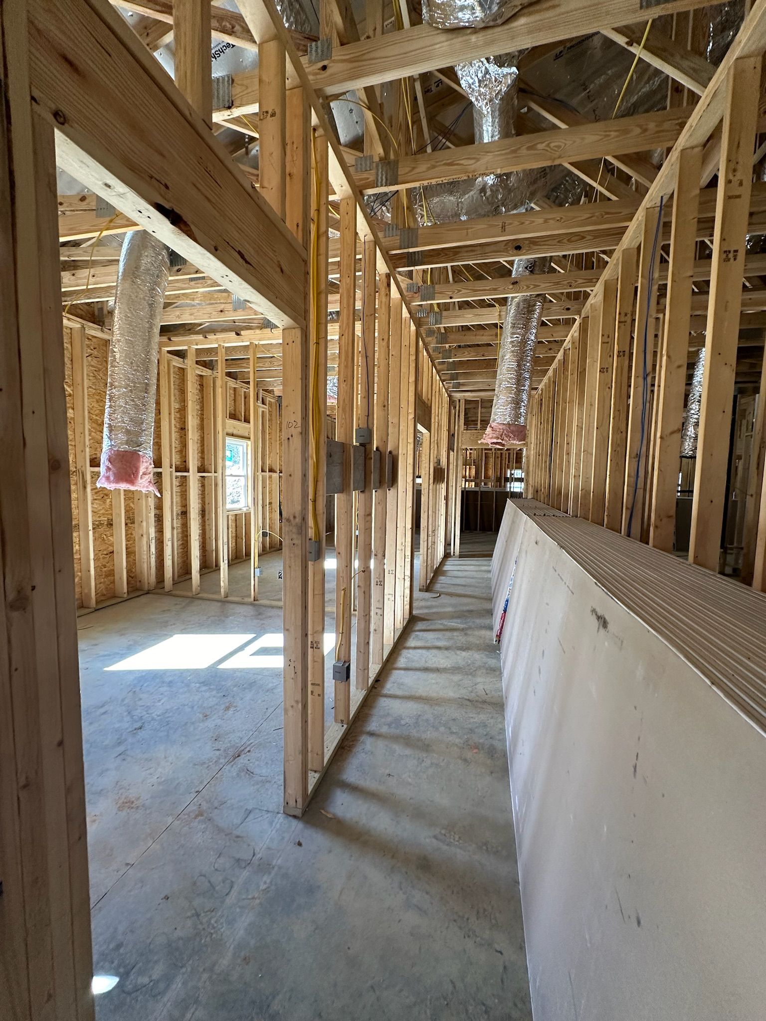 A long hallway in a building under construction with wooden beams and ducts hanging from the ceiling.