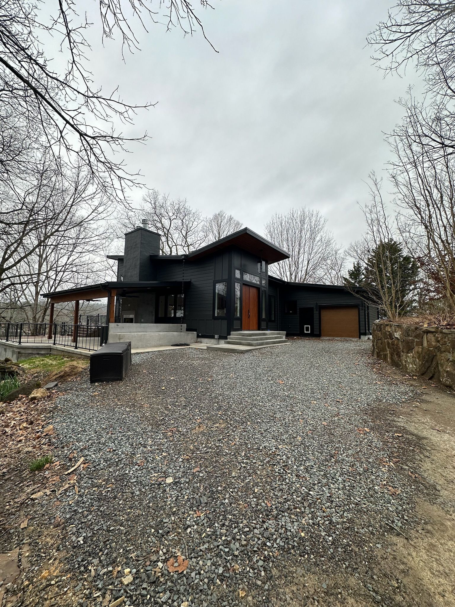 A black house with a gravel driveway in front of it.