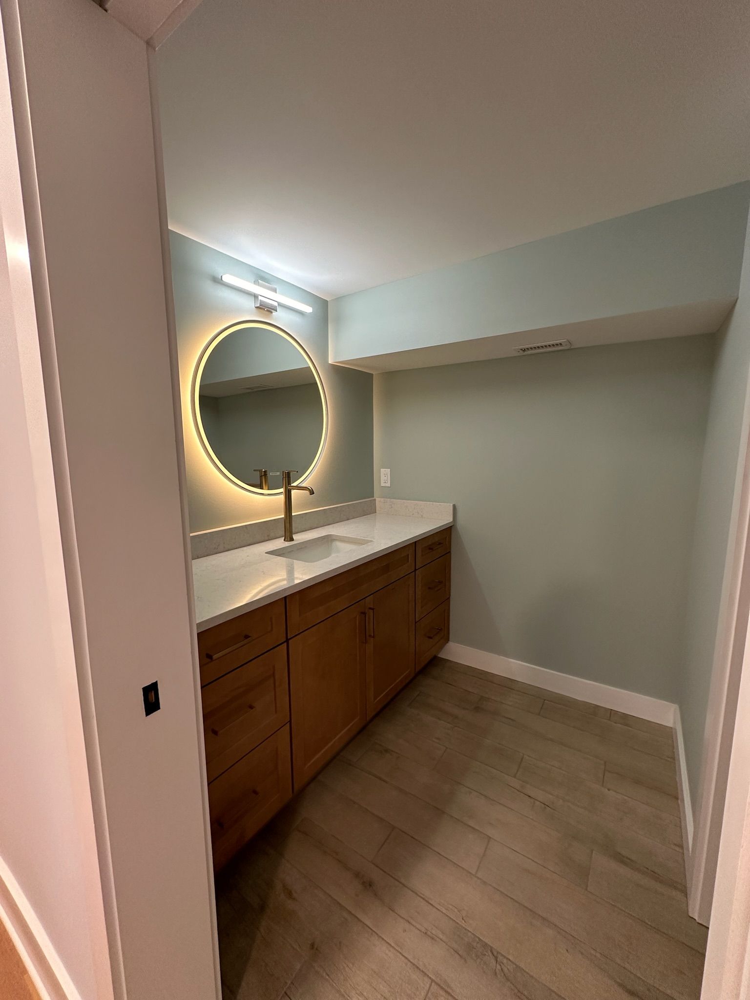 A bathroom with a sink , mirror and wooden cabinets.