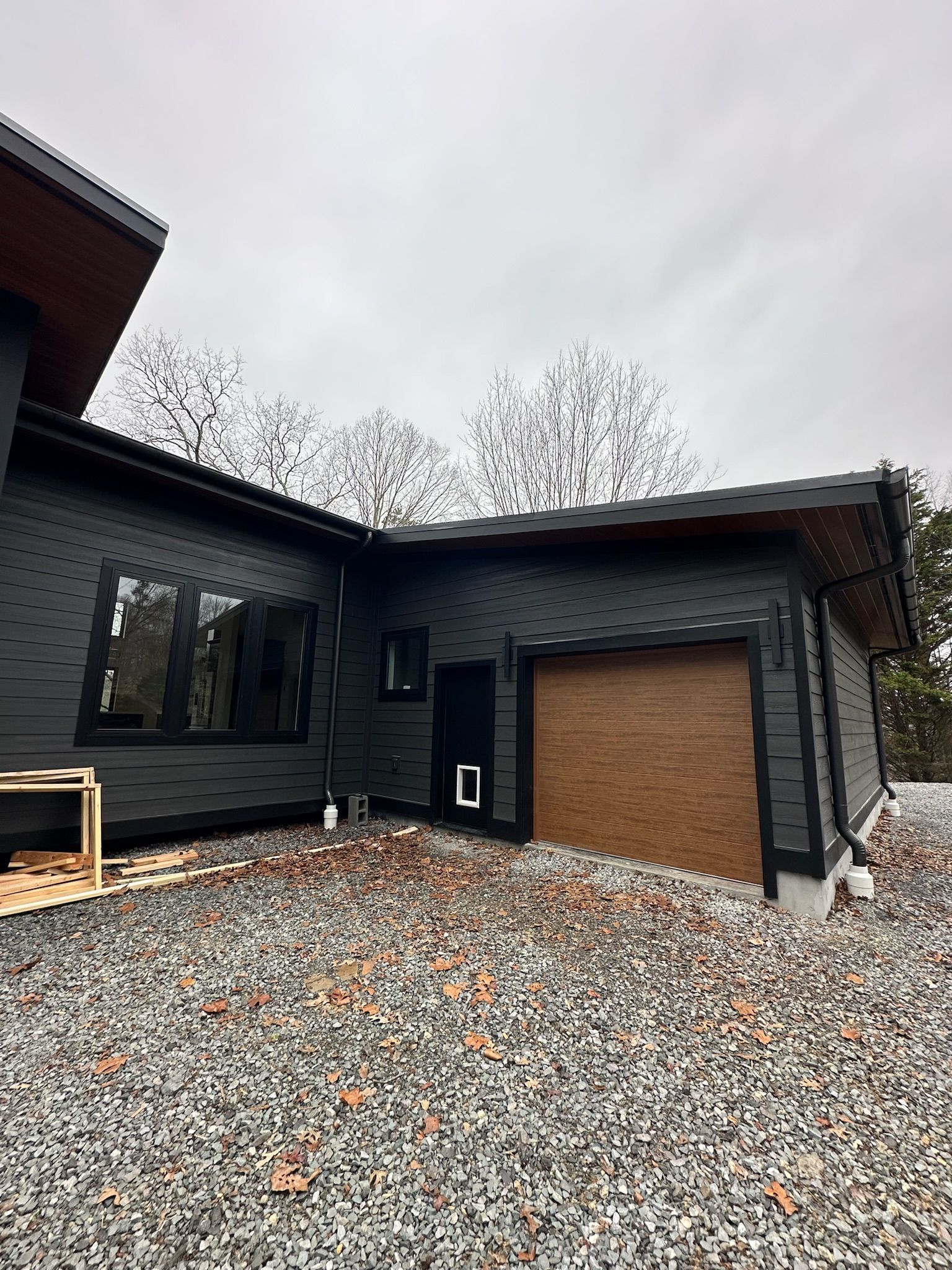 A black house with a garage door is sitting on top of a gravel hill.