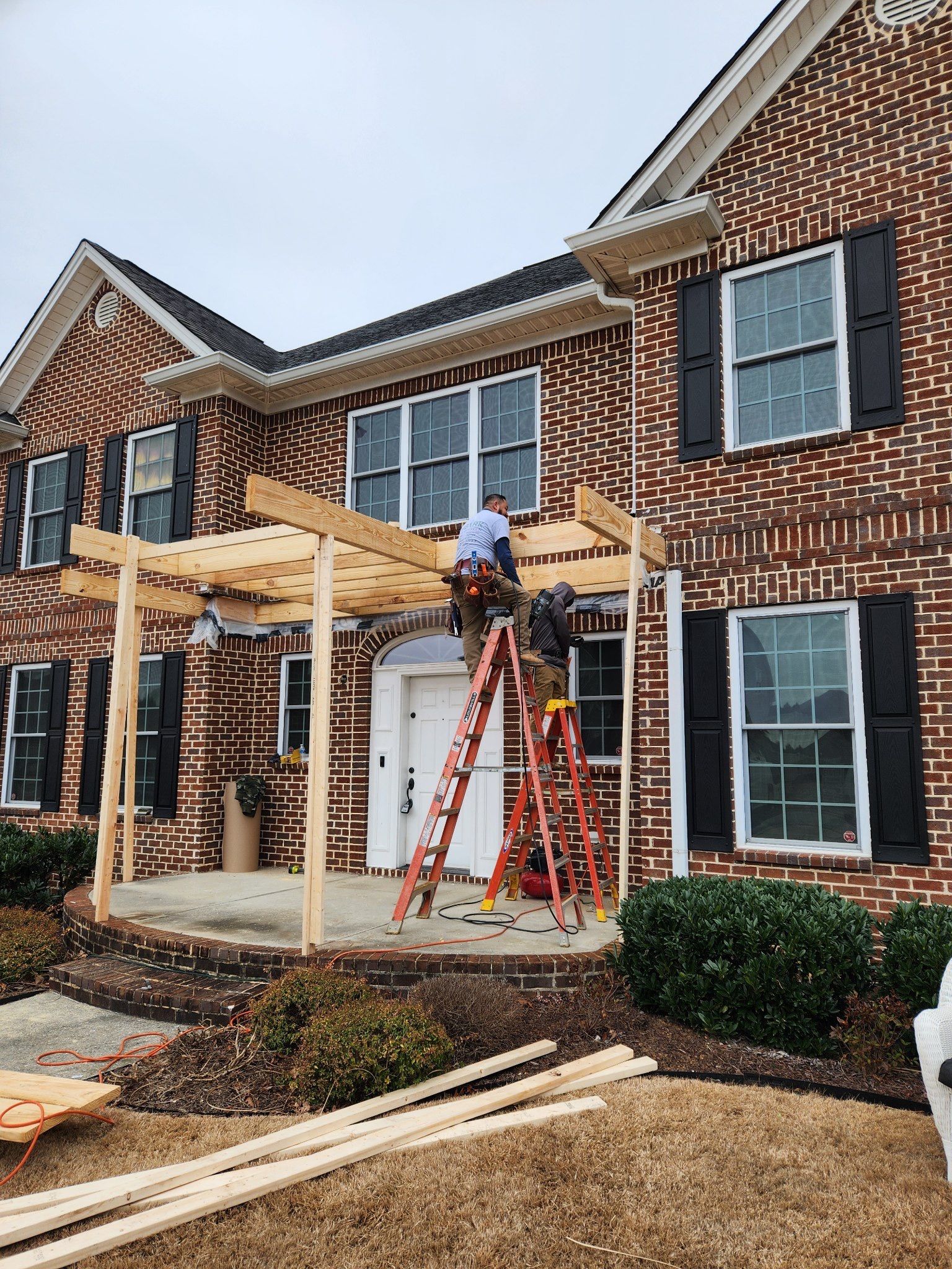A man is standing on a ladder in front of a brick house.
