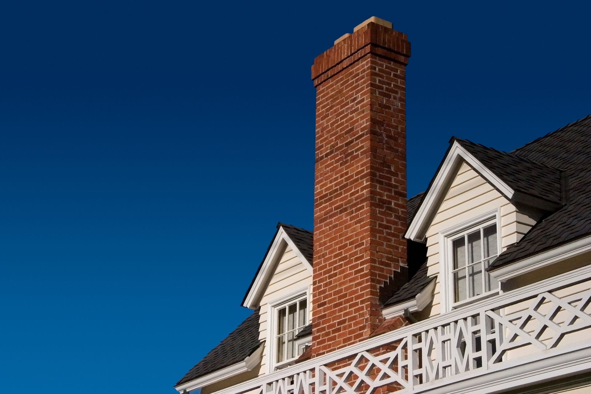 Brick chimney on a yellow-sided house with a black roof and a blue sky in the background.