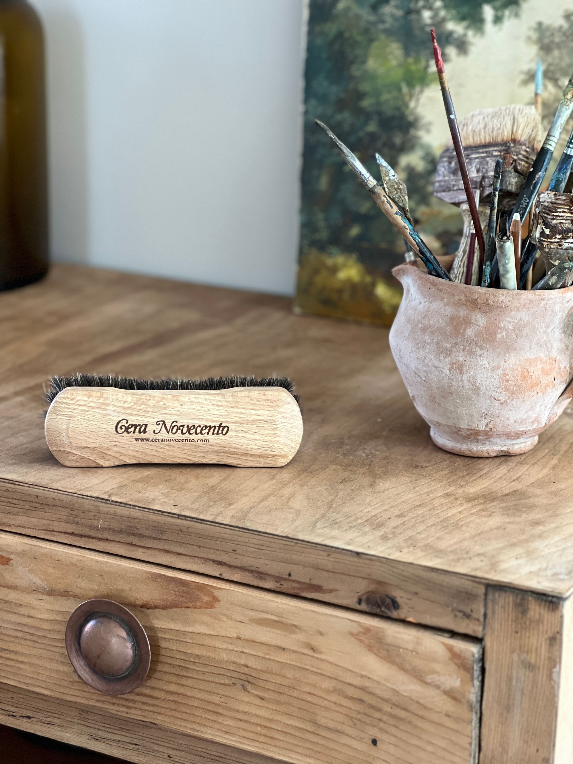 Tavolo da disegno in legno con un pennello, un vaso con pennelli e una bottiglia.