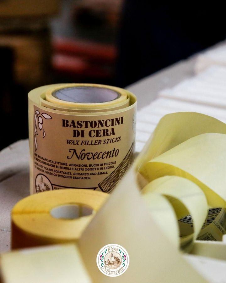 Un rotolo di stick di cera Novecento per la riparazione di mobili è appoggiato su una superficie chiara, con pezzi di nastro adesivo sparsi nelle vicinanze.