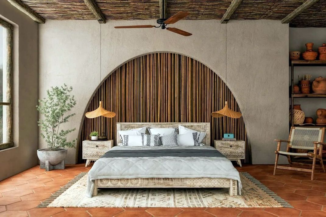 Una camera da letto con un letto posizionato al centro sotto un'ampia parete ad arco con doghe di legno, pavimento in cotto e arredamento rustico.