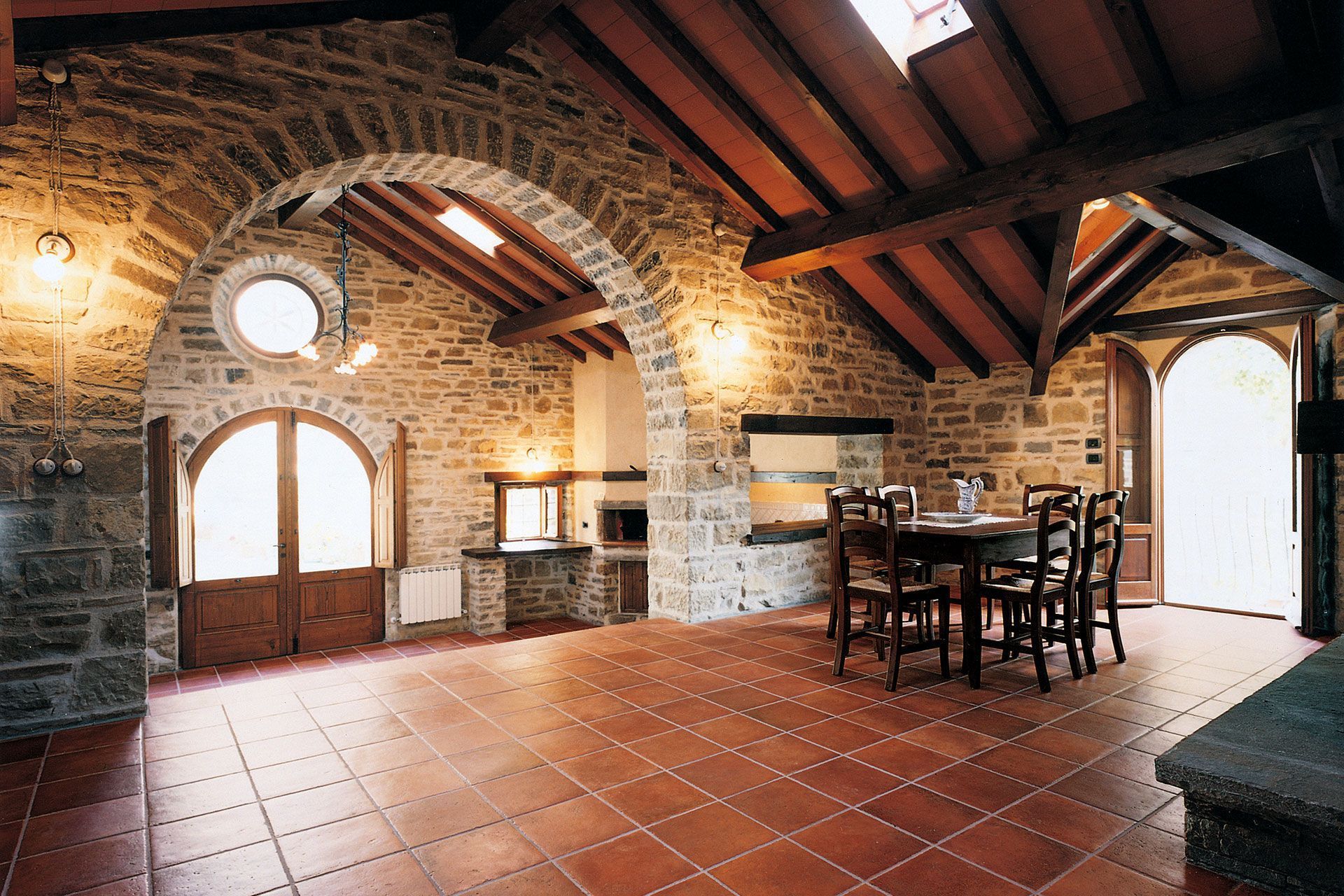 Sala da pranzo rustica con pareti in pietra, pavimento in piastrelle rosse e mobili in legno.