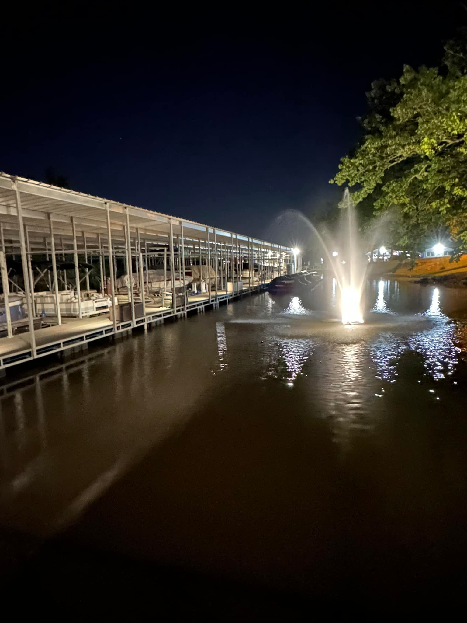 A fountain in the middle of a body of water next to a dock at night.