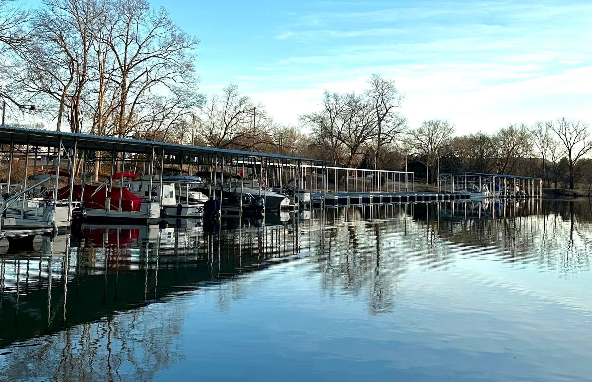 A row of boats are docked at a marina on a lake.