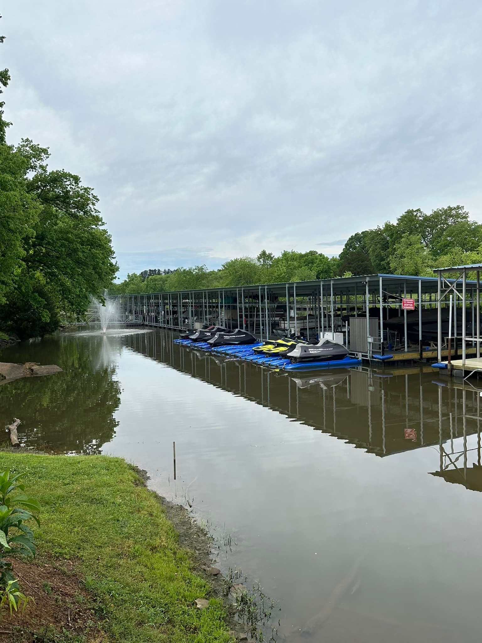 A row of boats are docked at a marina on a river.
