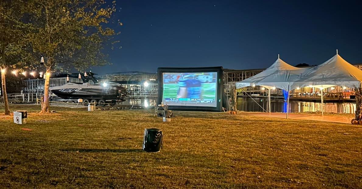 A large screen is sitting in the middle of a field at night.